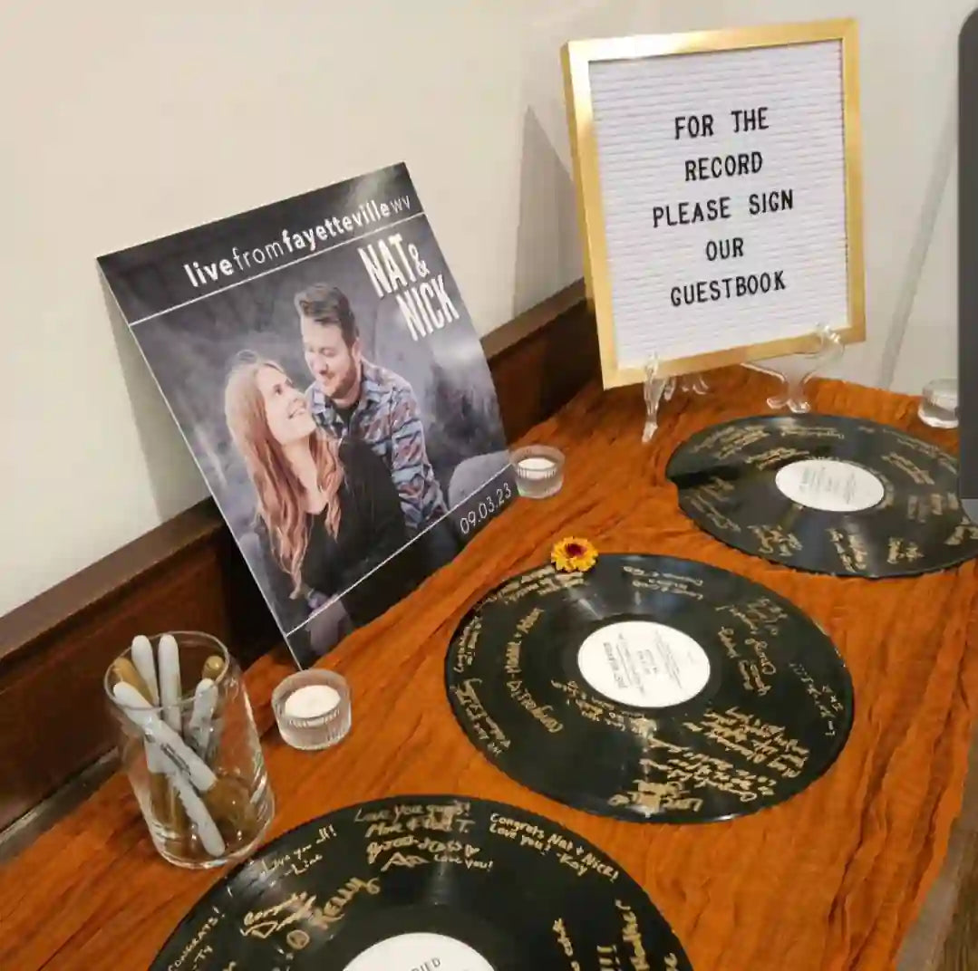Three personalized vinyl records used as a unique wedding guestbook, signed with gold markers by guests at a reception.
