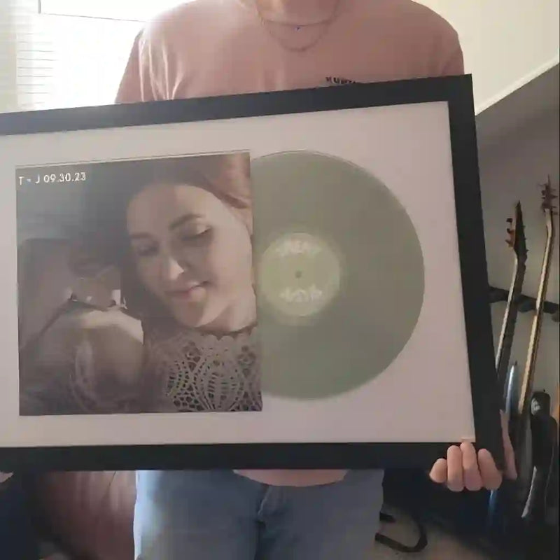 A sage green custom colored vinyl record professionally framed on a wall next to guitars, showing how a personalized photo record works as high-end home decor.