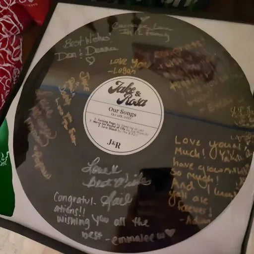 Close-up of a black vinyl record signed by wedding guests with gold metallic ink, showing high-resolution detail.