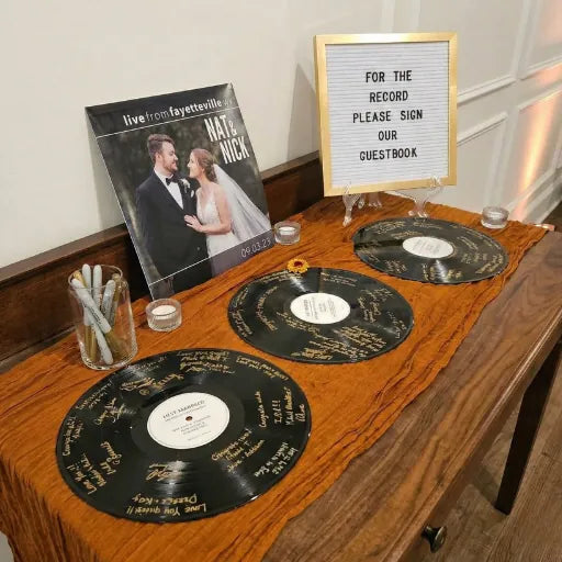 Stunning wedding welcome table with multiple signed vinyl records and a sign inviting guests to leave a message.